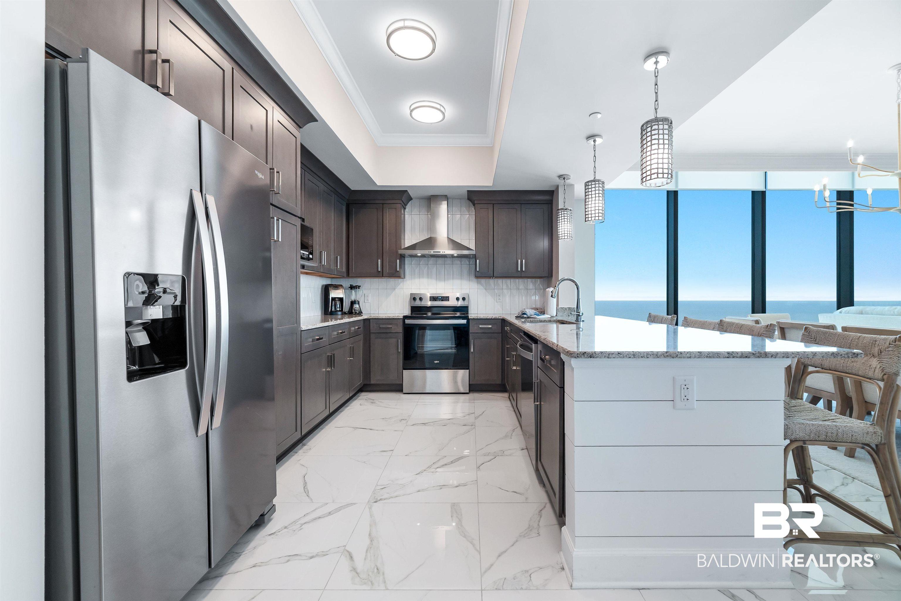 Image 3: Modern kitchen featuring stainless steel appliances, dark wood cabinetry, white granite countertops, and white tile flooring