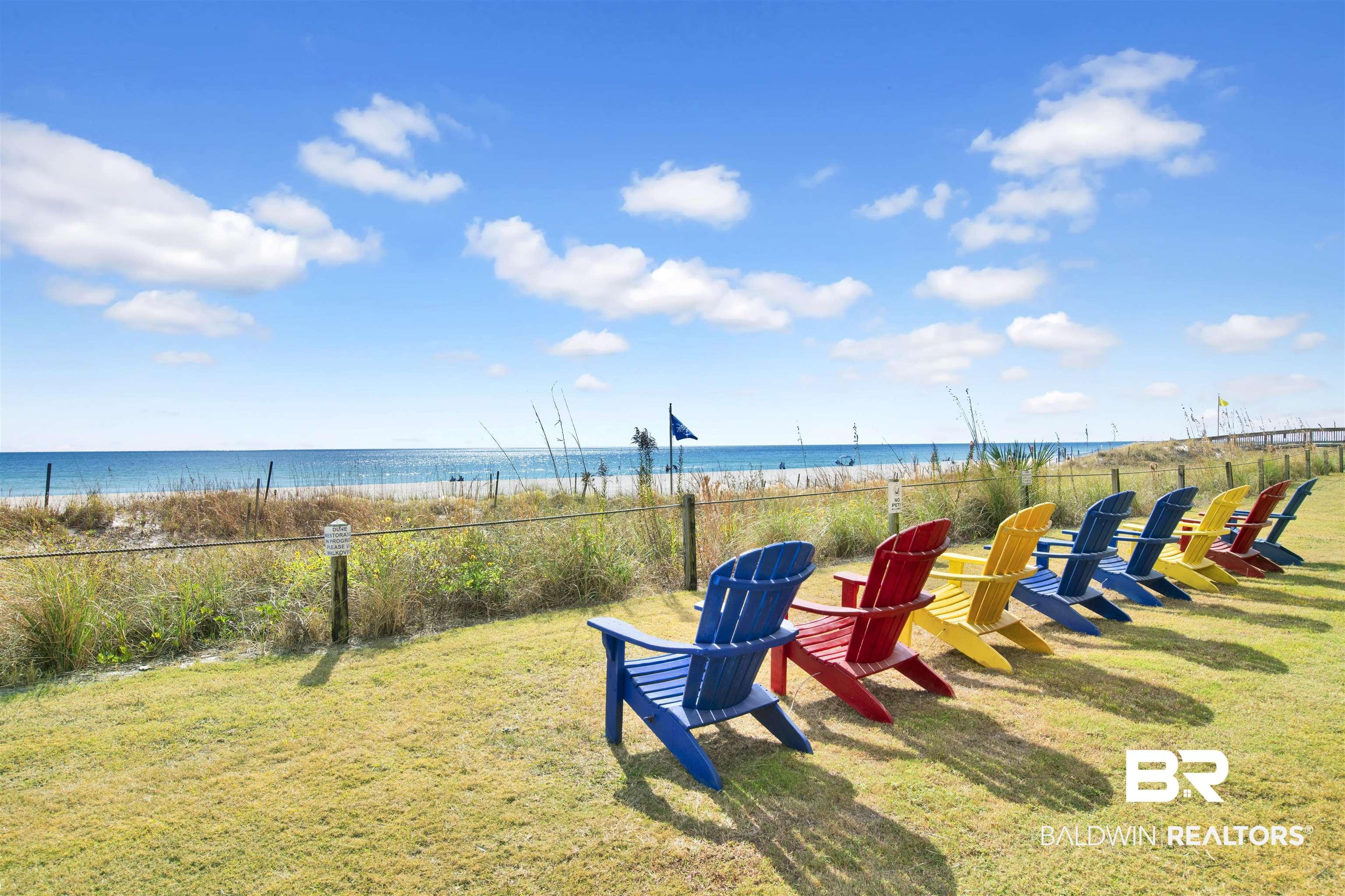 Image 3: Expansive lawn area featuring a row of colorful Adirondack chairs, a natural dune barrier, and direct beachfront access