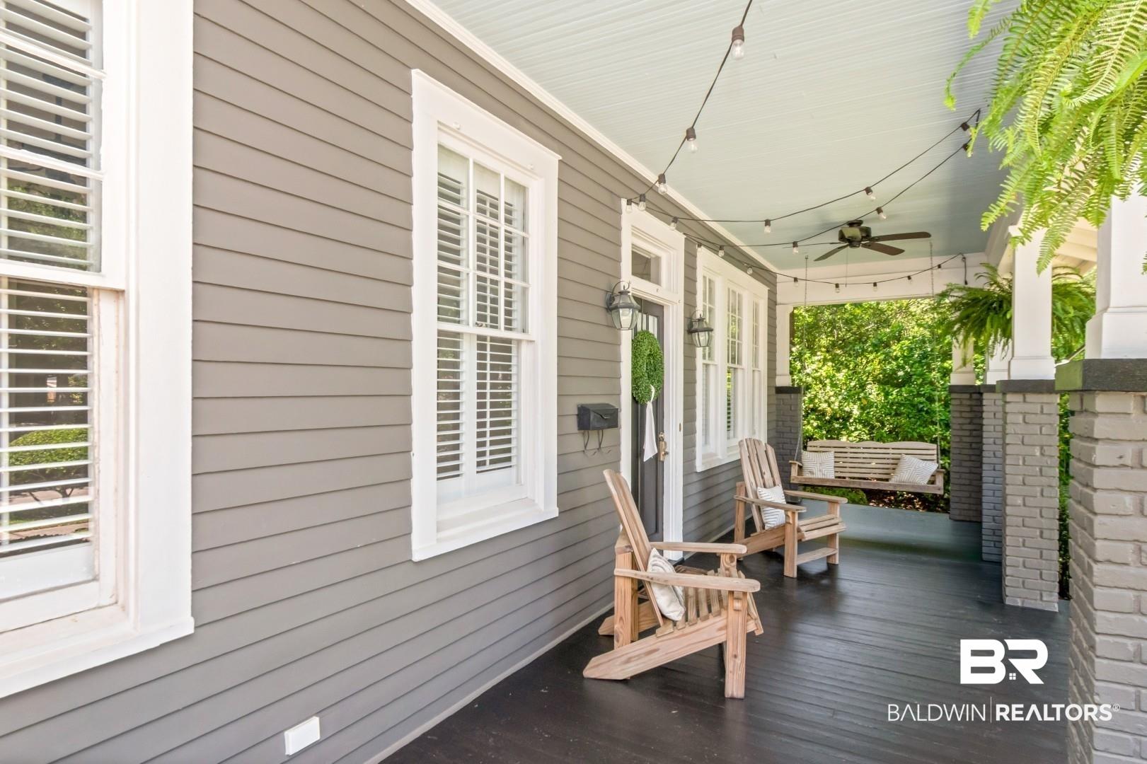 Image 2: Inviting front porch featuring a dark wood-finish floor, light gray siding, white trim windows with interior shutters, and painted brick columns