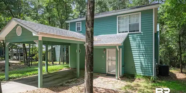 Image 3: Exterior featuring green horizontal siding, a carport with a gable roof, and a white entry door