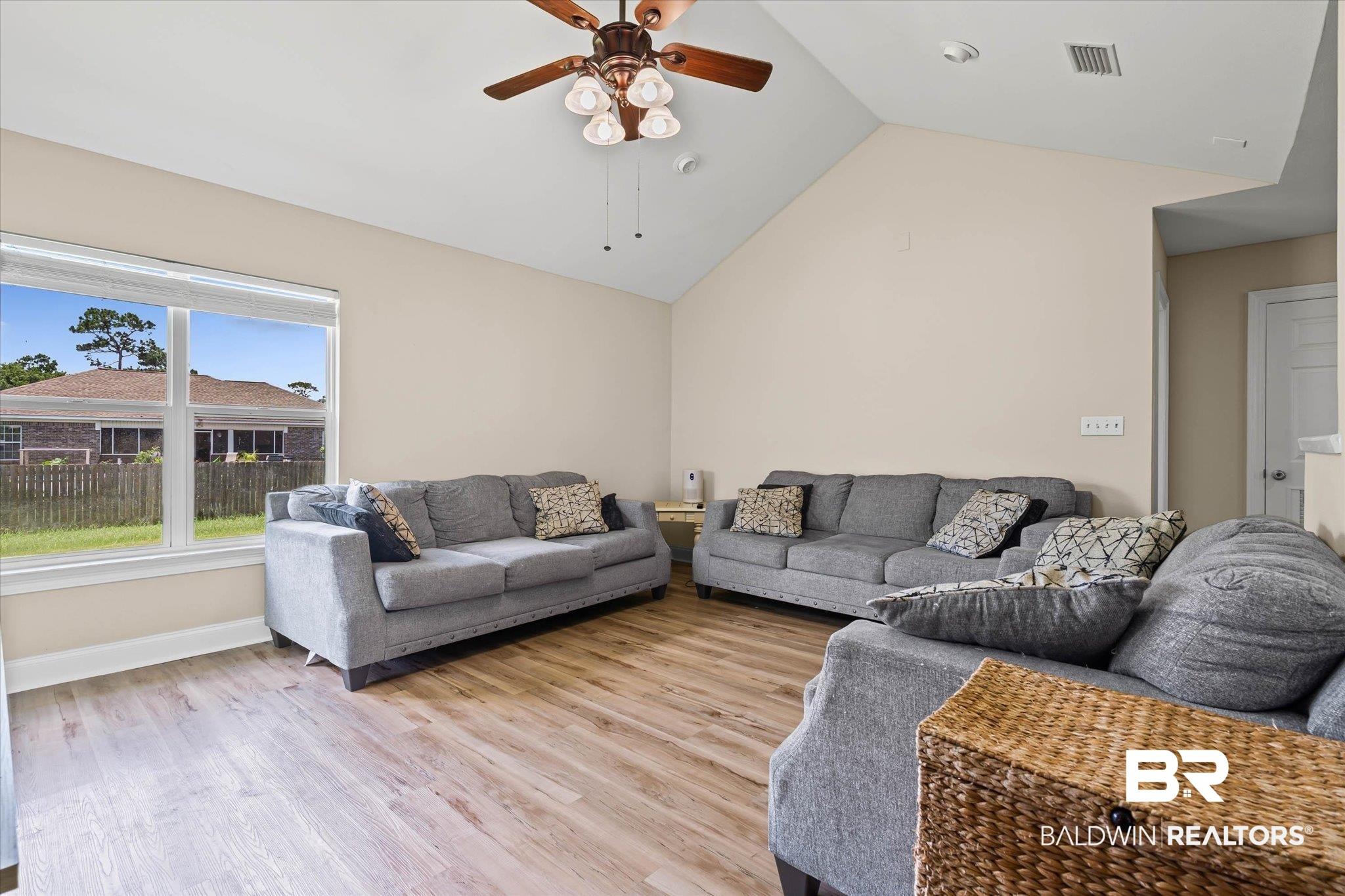 Image 3: Vaulted ceiling with a ceiling fan light fixture, wood-finish flooring, and a large window providing natural light