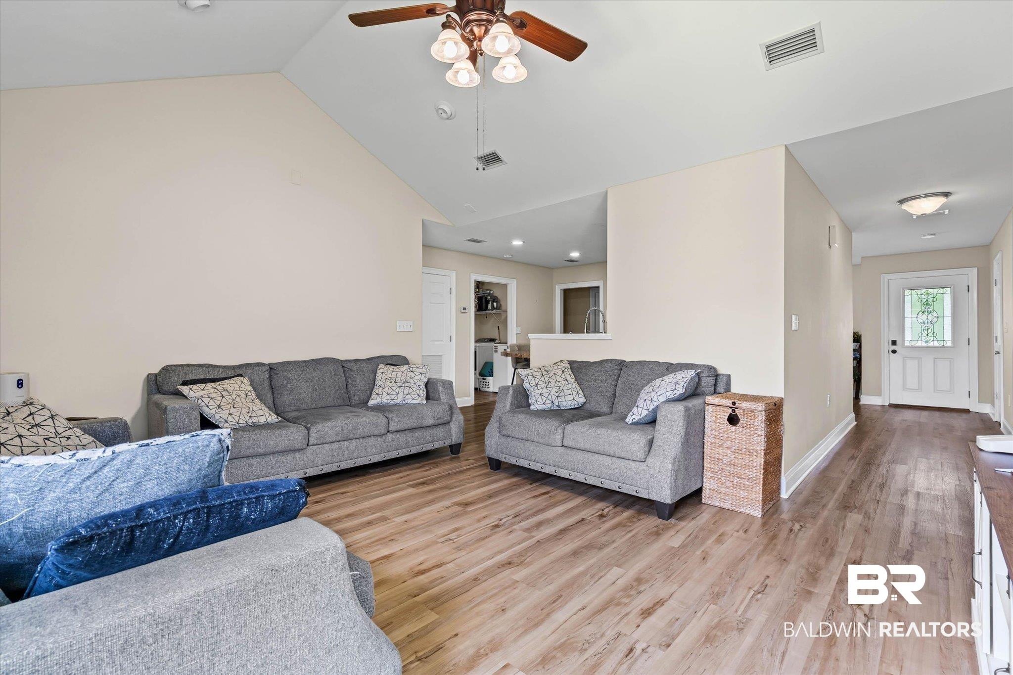 Image 4: Open-concept living area featuring wood-finish flooring, vaulted ceilings, and a ceiling fan with integrated lighting
