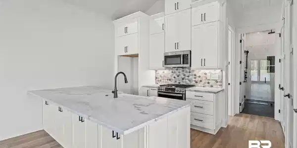Image 4: Kitchen with white cabinetry, stainless steel appliances, light stone counters, backsplash, and light wood-style floors