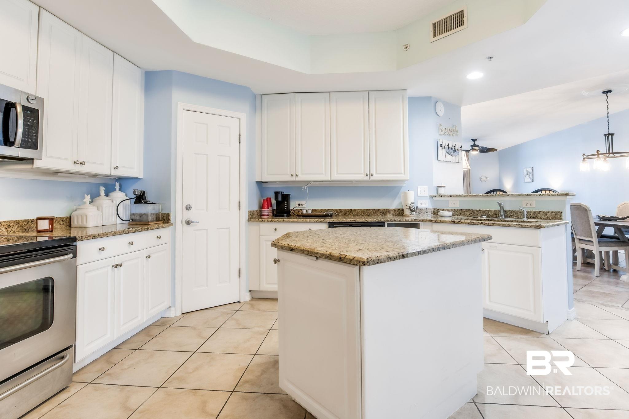 Image 3: Kitchen featuring appliances with stainless steel finishes, a kitchen island, light tile patterned floors, a peninsula, and light stone countertops