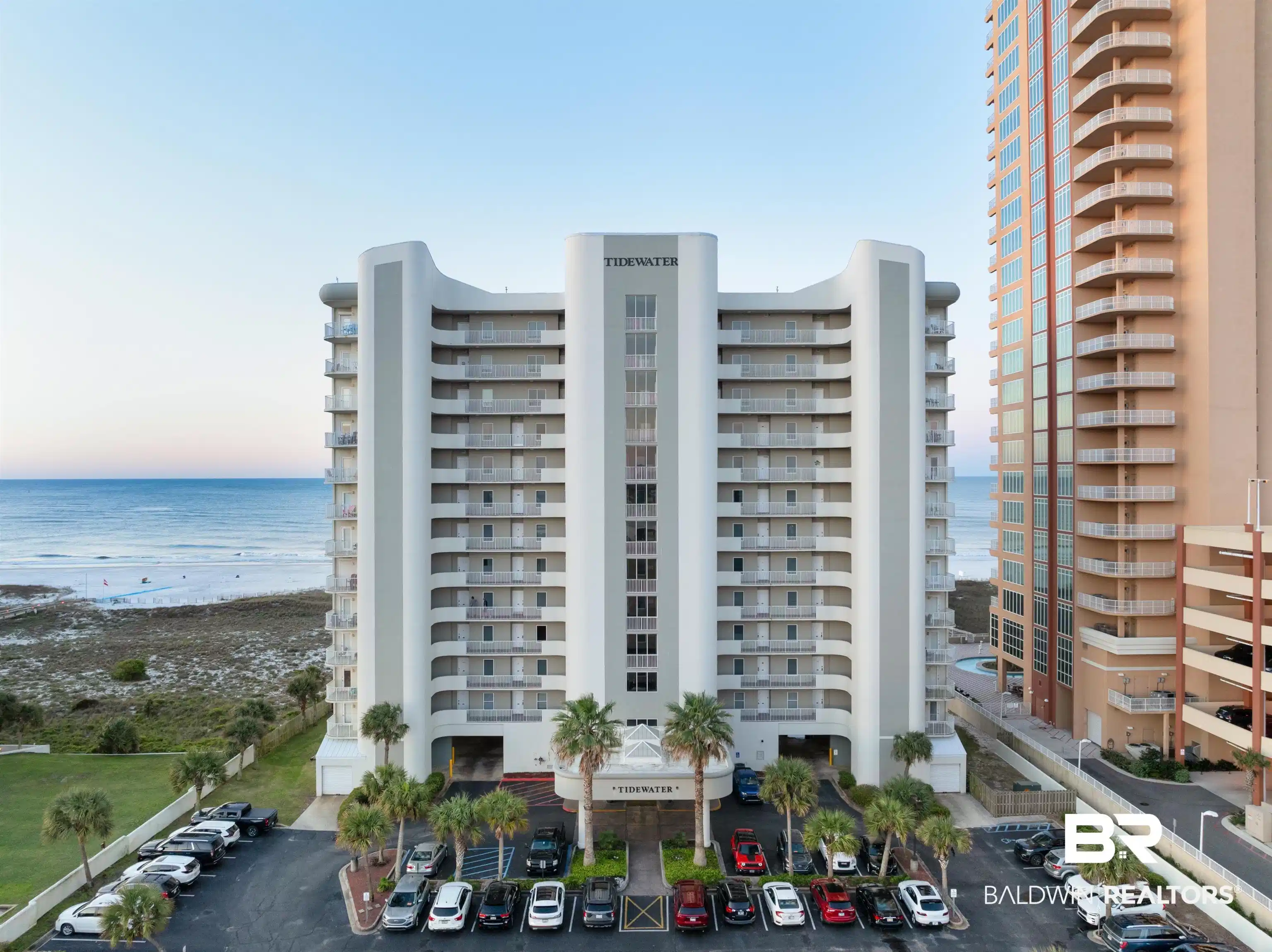 Image 1: Property at dusk with a view of apartment building / complex, view of water and beach, and uncovered parking