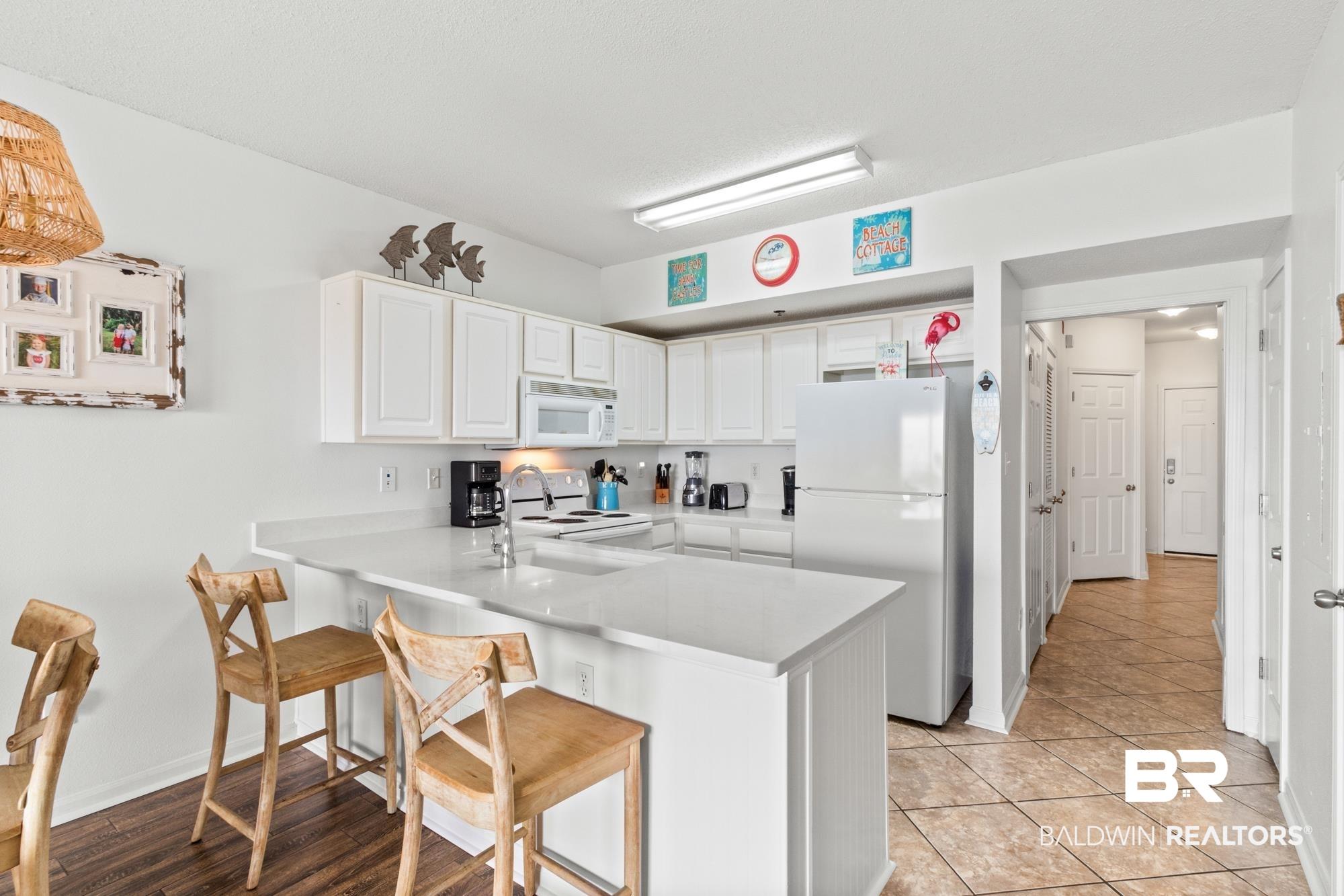 Image 3: Kitchen with white cabinetry, a breakfast bar, white appliances, and kitchen peninsula