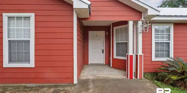 Image 2: Red horizontal siding exterior with a covered entry, white front door, and multiple windows featuring white trim