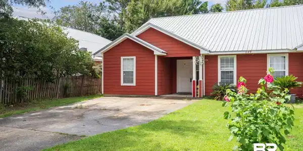 Image 3: Red-sided exterior featuring a silver metal roof, white trim windows, and a paved driveway