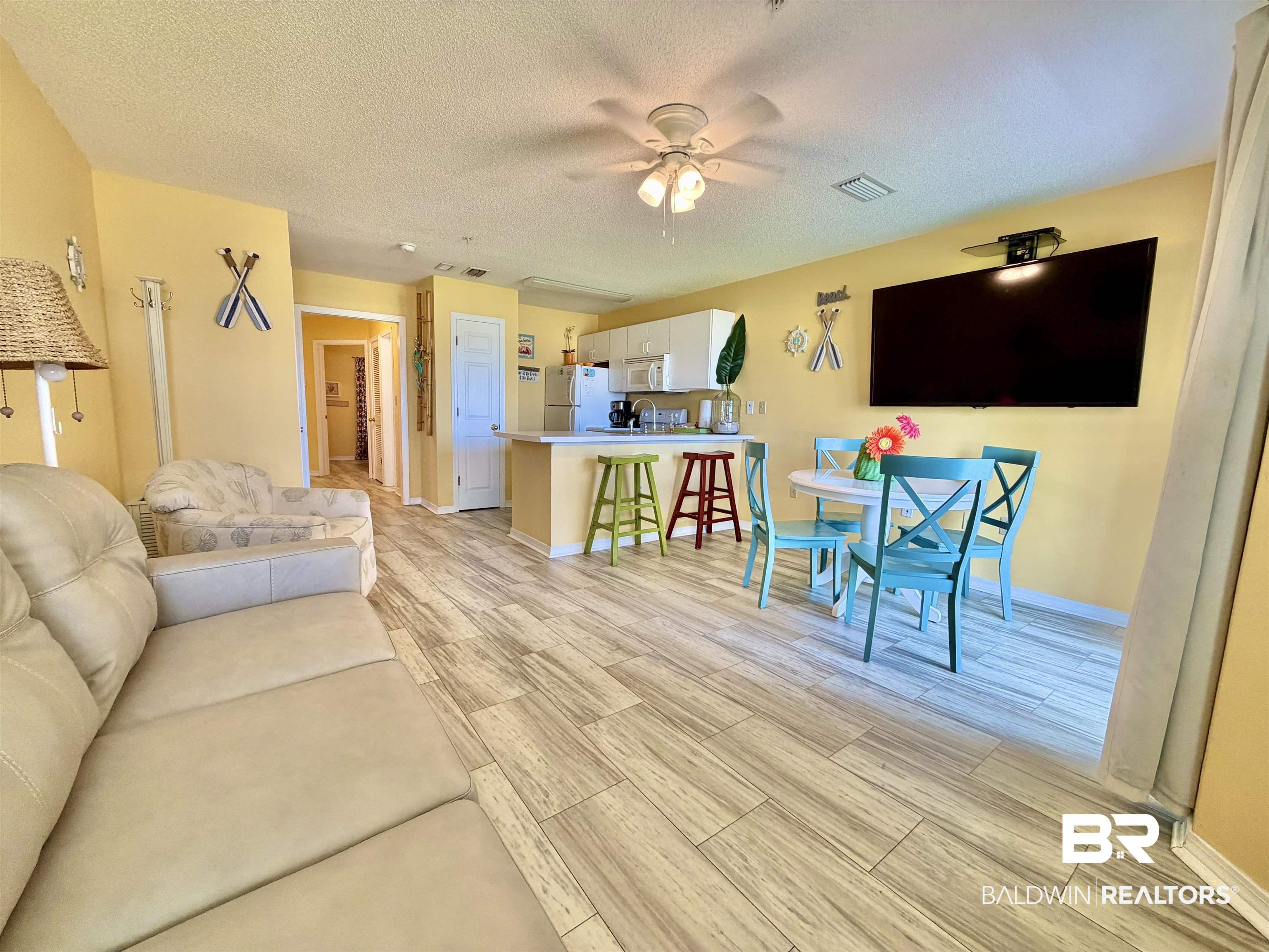 Image 4: Open-concept living area featuring wood-finish flooring, a ceiling fan with integrated lighting, and a neutral wall color