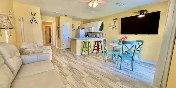 Image 4: Open-concept living area featuring wood-finish flooring, a ceiling fan with integrated lighting, and a neutral wall color