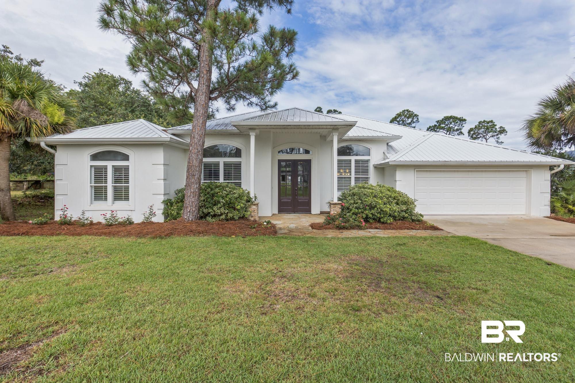 Image 2: White stucco exterior featuring a metal roof, arched windows with plantation shutters, a double-door entry, and an attached two-car garage