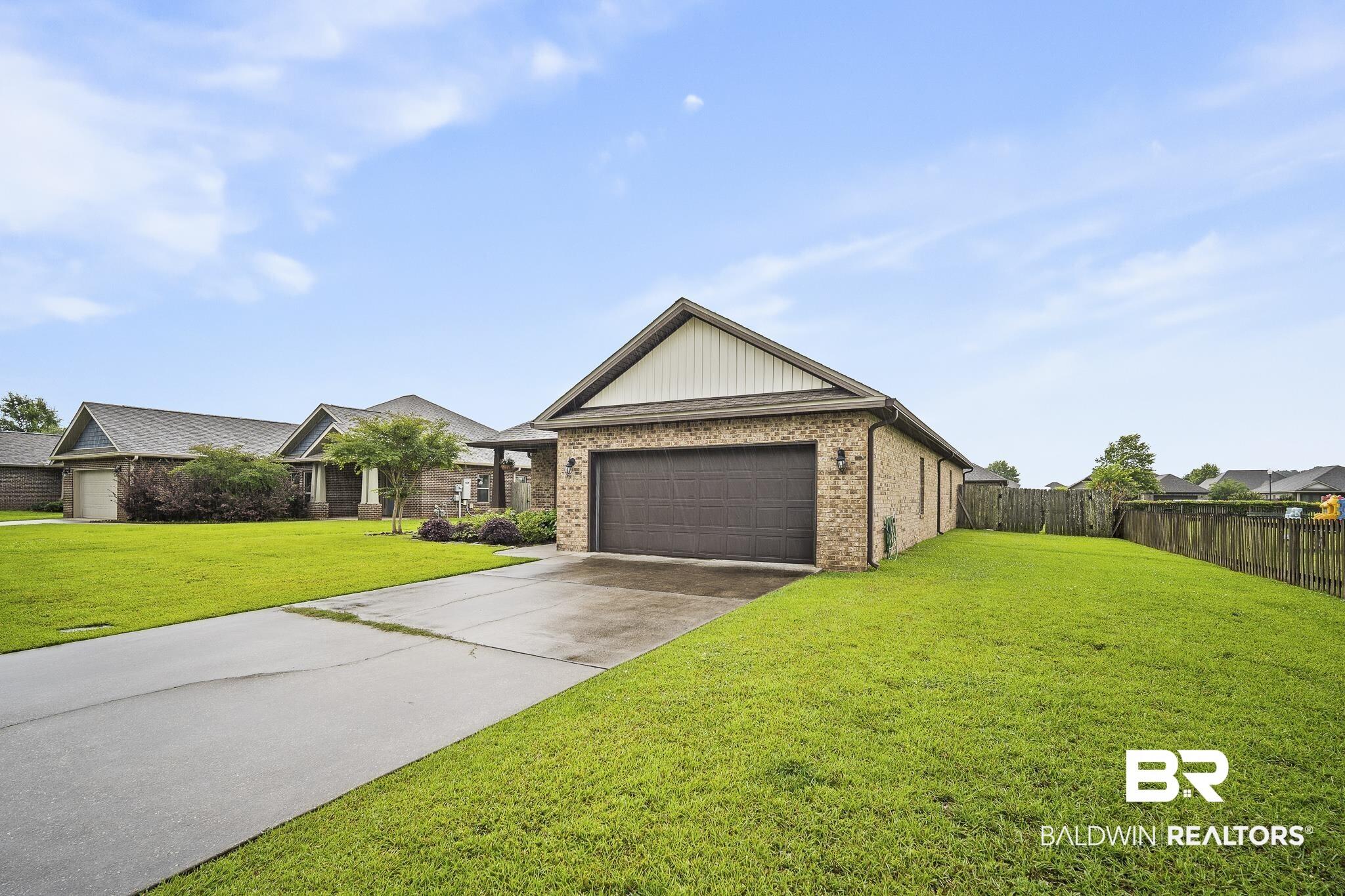 Image 2: Brick exterior residence featuring an attached garage with a dark panel door, a paved driveway, and a wooden privacy fence