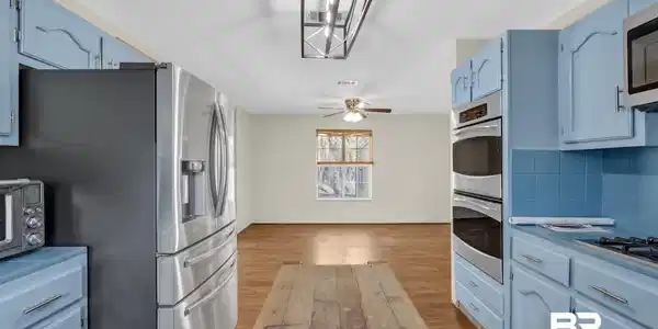 Image 4: Kitchen featuring blue cabinets, stainless steel appliances, light wood-type flooring, light countertops, and suspended lighting