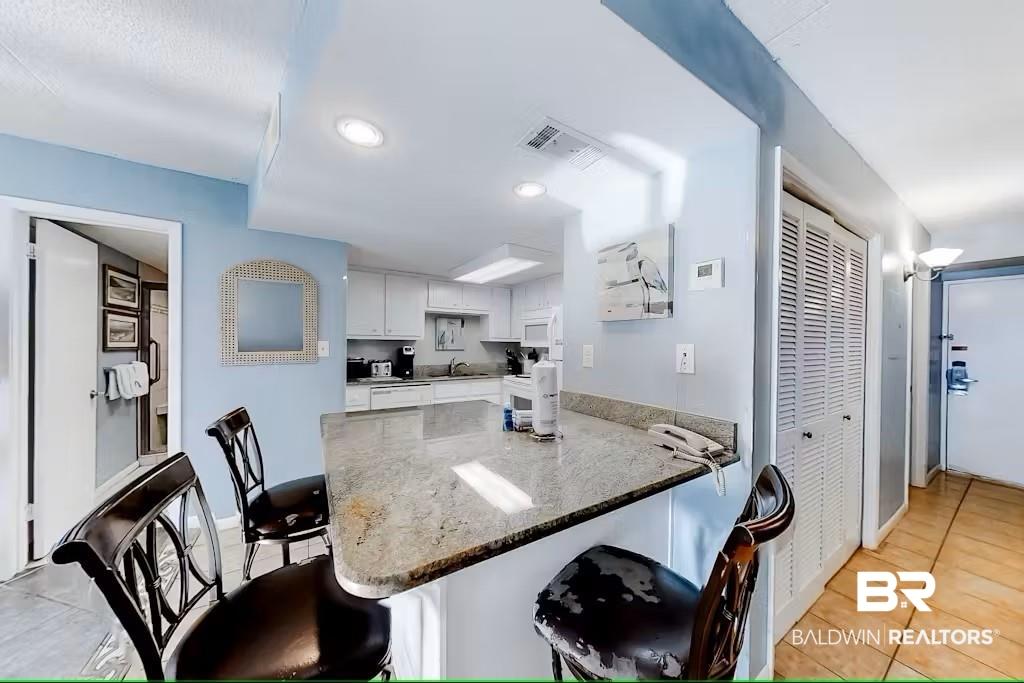 Image 2: Kitchen with white cabinetry, kitchen peninsula, dark stone countertops, and a kitchen bar