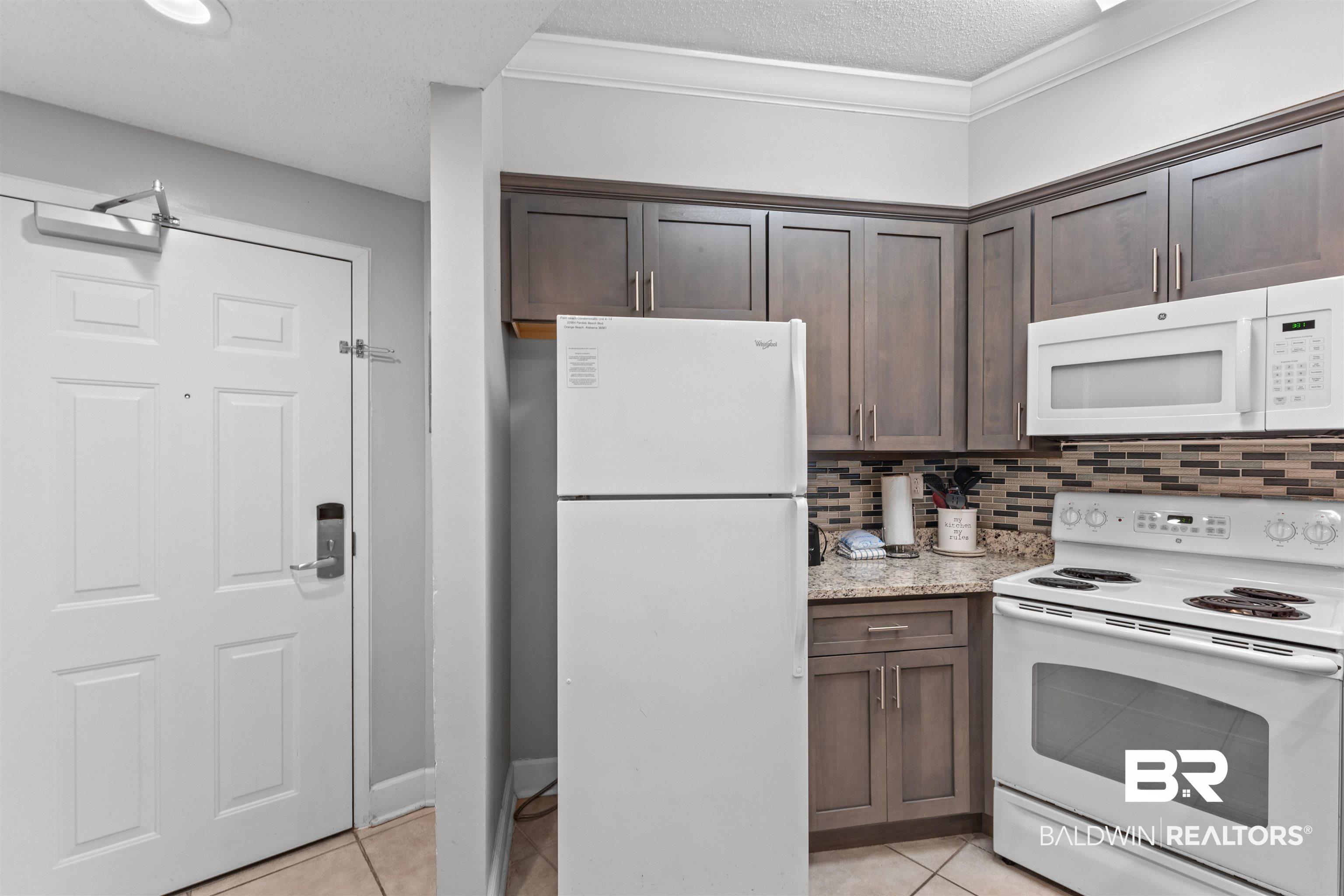 Image 4: Kitchen featuring white appliances, dark brown cabinets, light tile patterned flooring, a textured ceiling, and crown molding