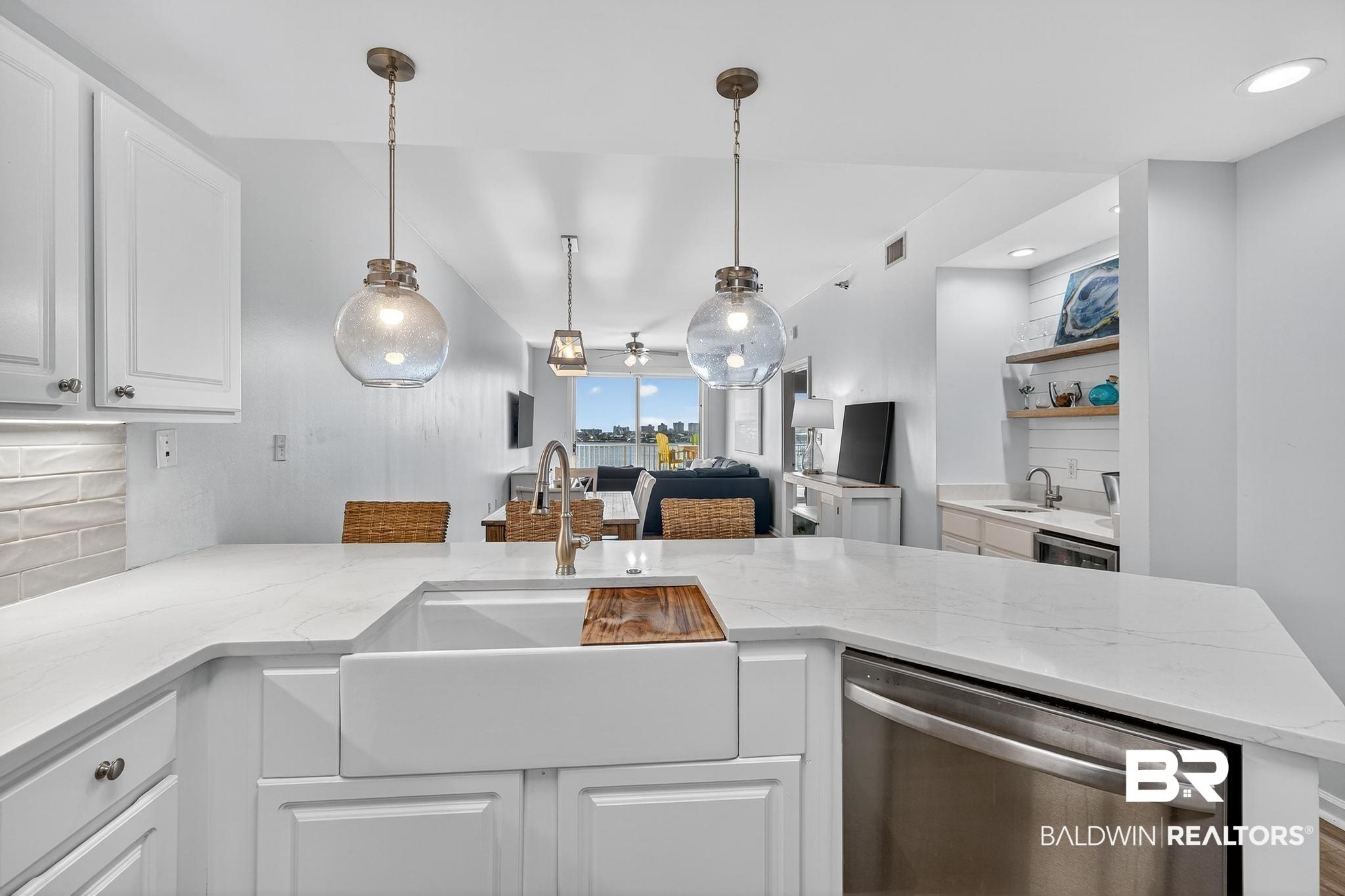 Image 4: Kitchen featuring white cabinets, light stone counters, open floor plan, stainless steel dishwasher, and tasteful backsplash