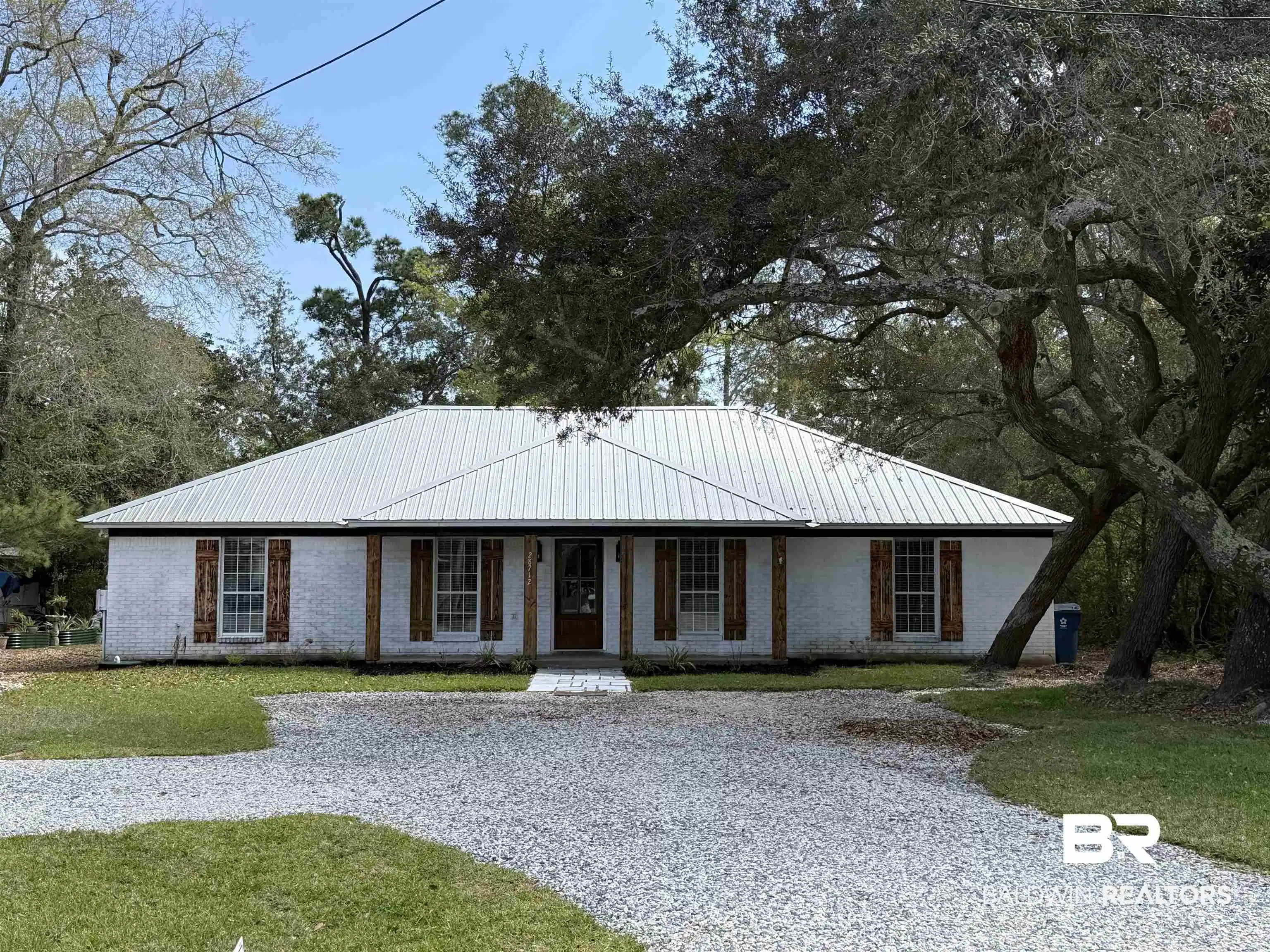 Image 1: Single story home with brick siding, a metal roof, a front lawn, and a porch