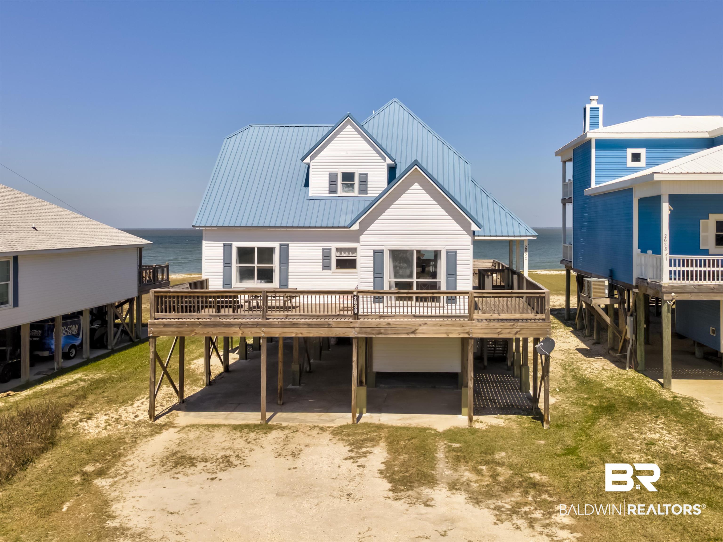 Image 1: Back of property with a deck with water view, a carport, a metal roof, and driveway