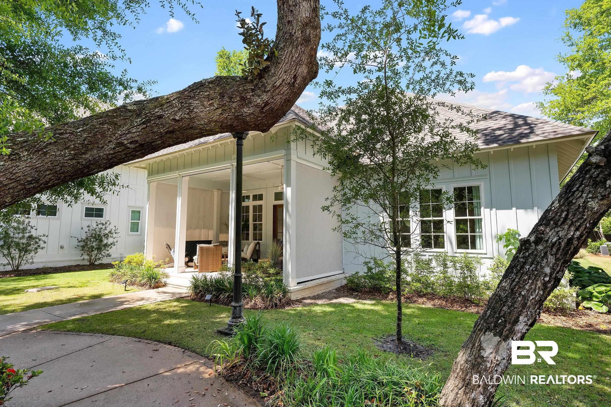 Image 3: Exterior featuring a covered patio, board and batten siding, multiple windows with white trim, a shingle roof, and a mature tree providing natural shade