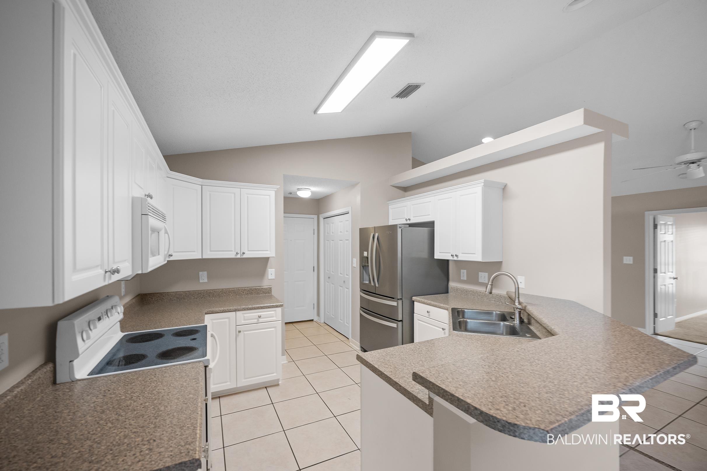 Image 2: Kitchen featuring white cabinetry, speckled countertops, stainless steel appliances, and tile flooring