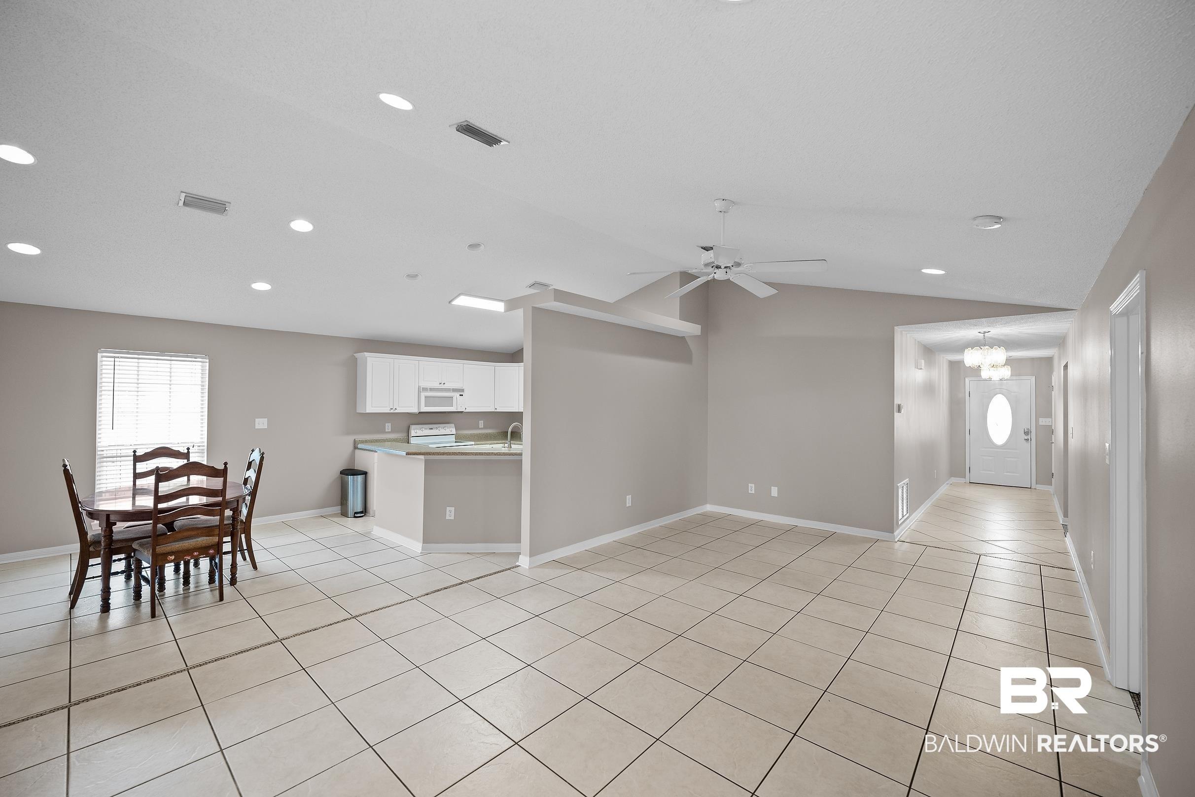 Image 3: Spacious living area featuring light-toned tile flooring, vaulted ceilings, and recessed lighting