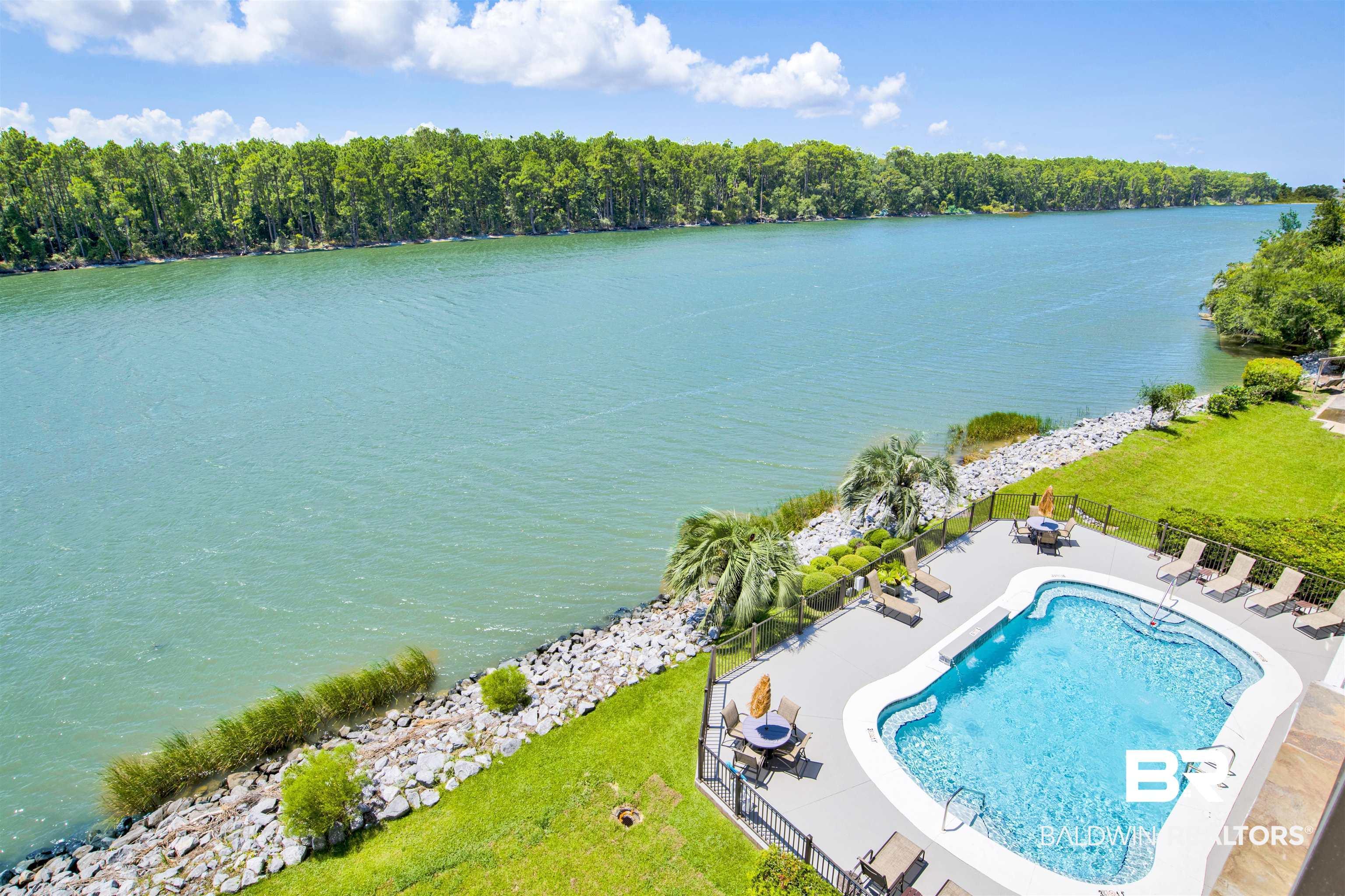 Image 3: Riverside property featuring a fenced swimming pool with a paved deck, mature palm trees, manicured lawns, and a riprap shoreline