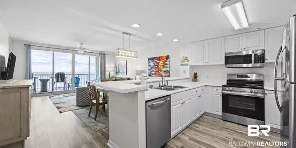 Image 3: Open-concept living area with wood-finish flooring, white cabinetry, stainless steel appliances, and a balcony with waterfront scenery