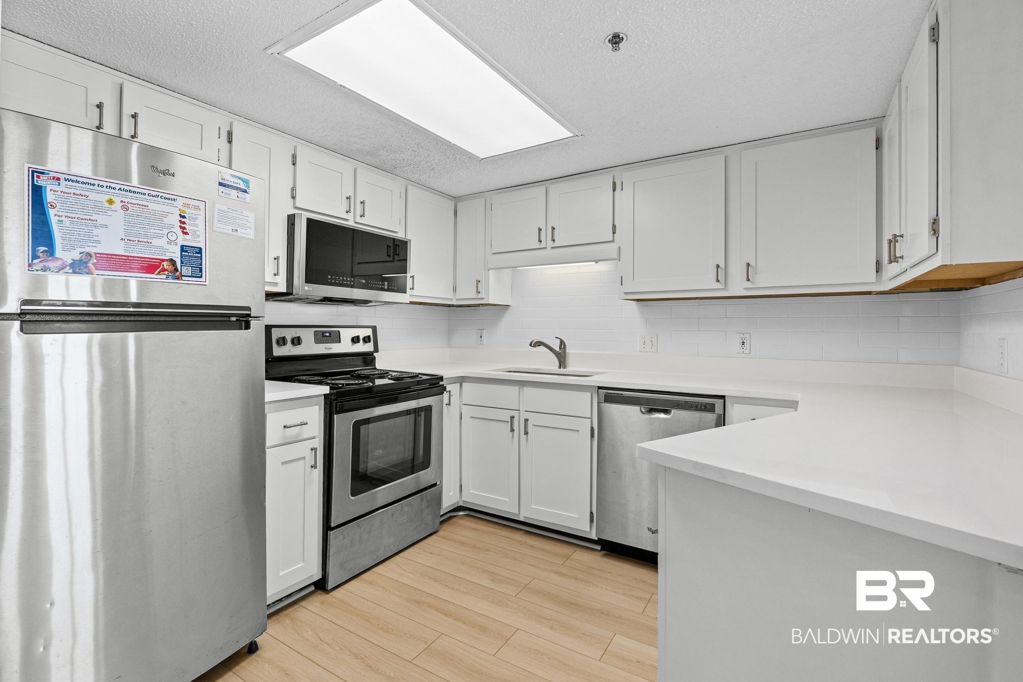 Image 3: Renovated kitchen featuring white cabinetry, light countertops, wood-finish flooring, stainless steel appliances, and a subway tile backsplash