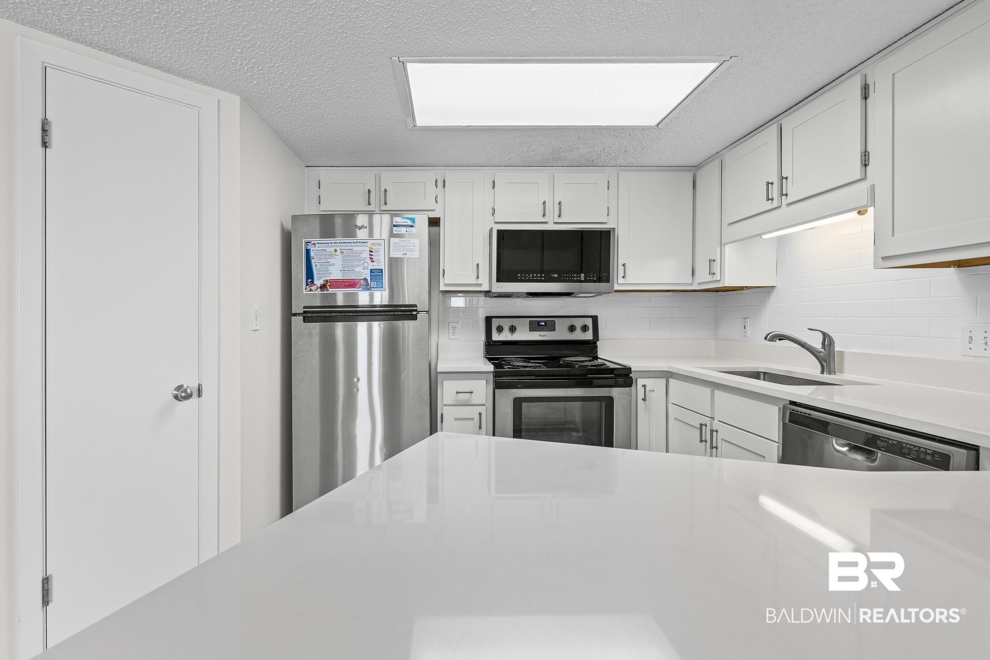 Image 4: Kitchen with white cabinetry, stainless steel appliances, white subway tile backsplash, and light-toned countertops