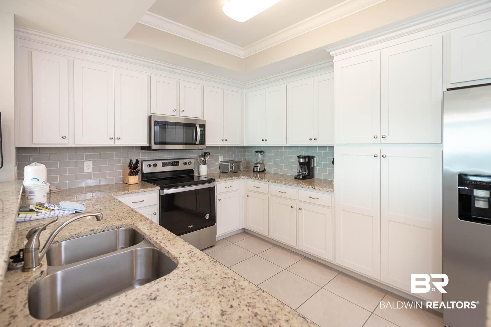 Image 4: Kitchen with appliances with stainless steel finishes, white cabinetry, tasteful backsplash, light tile patterned flooring, and crown molding