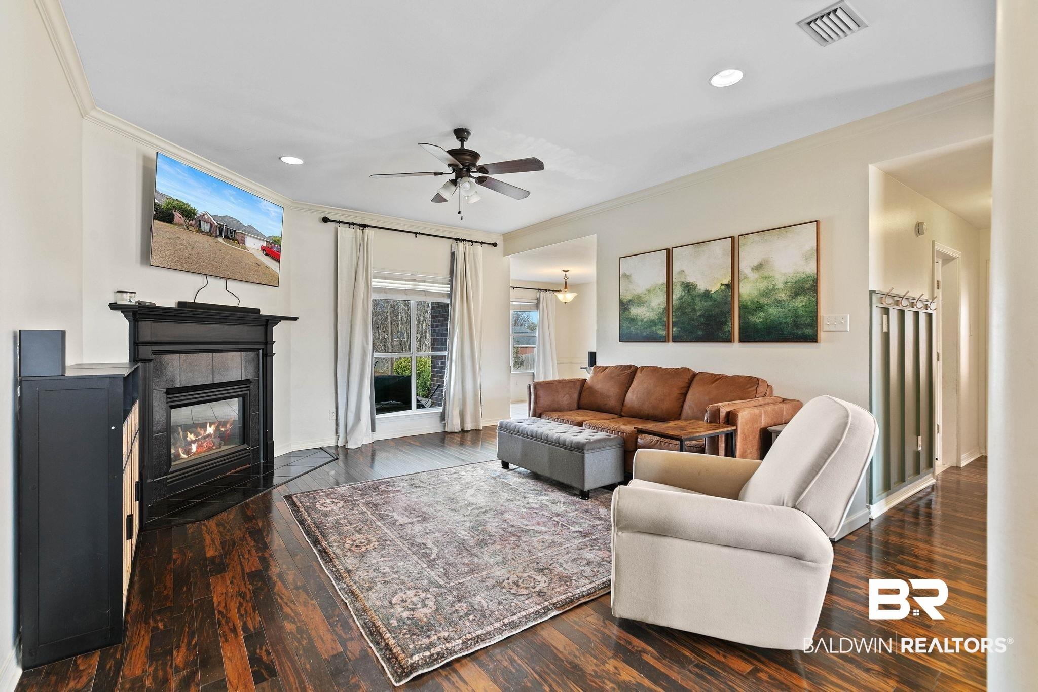 Image 4: Living room with ceiling fan, recessed lighting, dark wood-style floors, a tiled fireplace, and ornamental molding