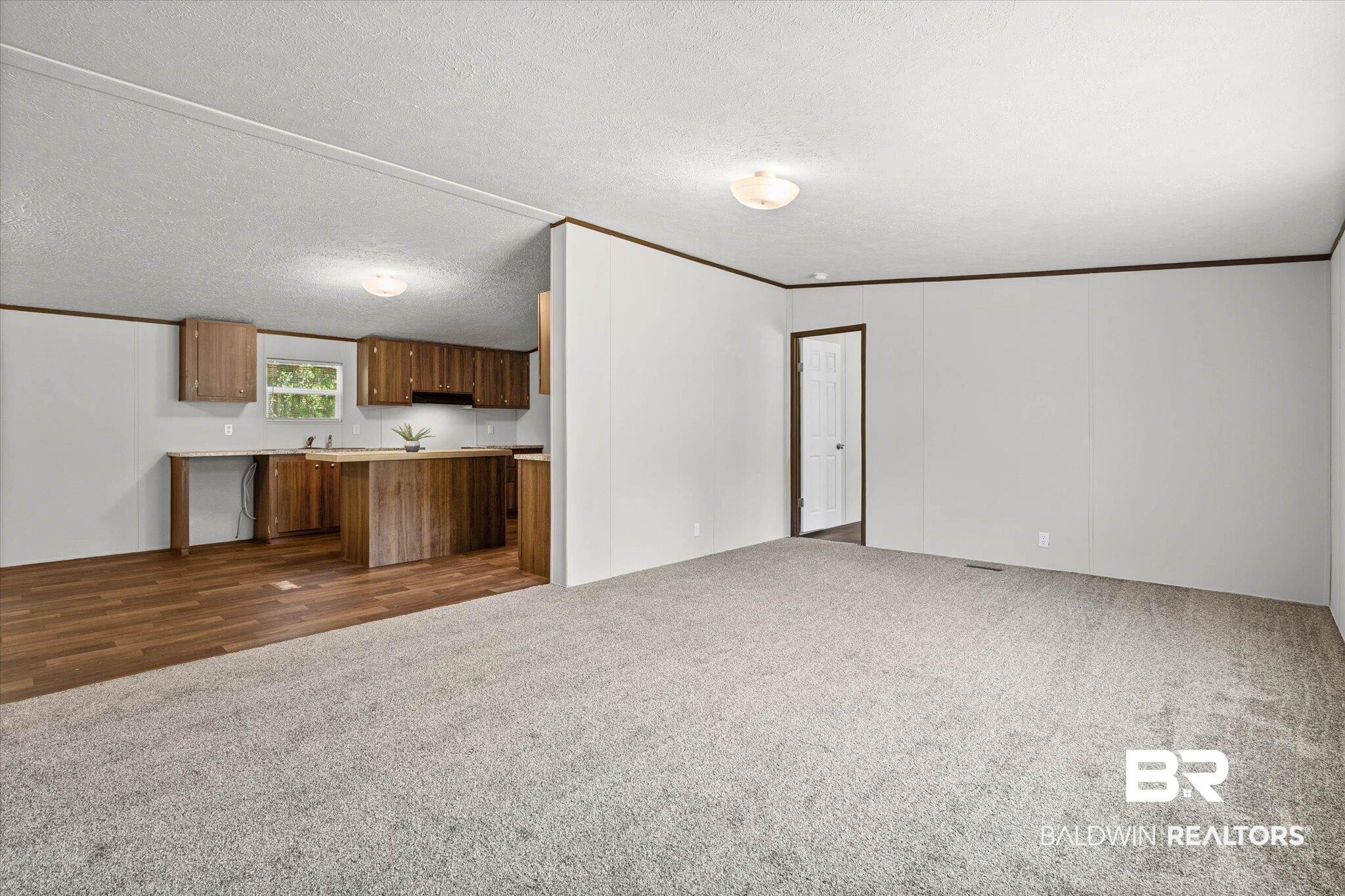 Image 2: Open concept living area with carpeting, wood-finish flooring, and natural wood cabinetry