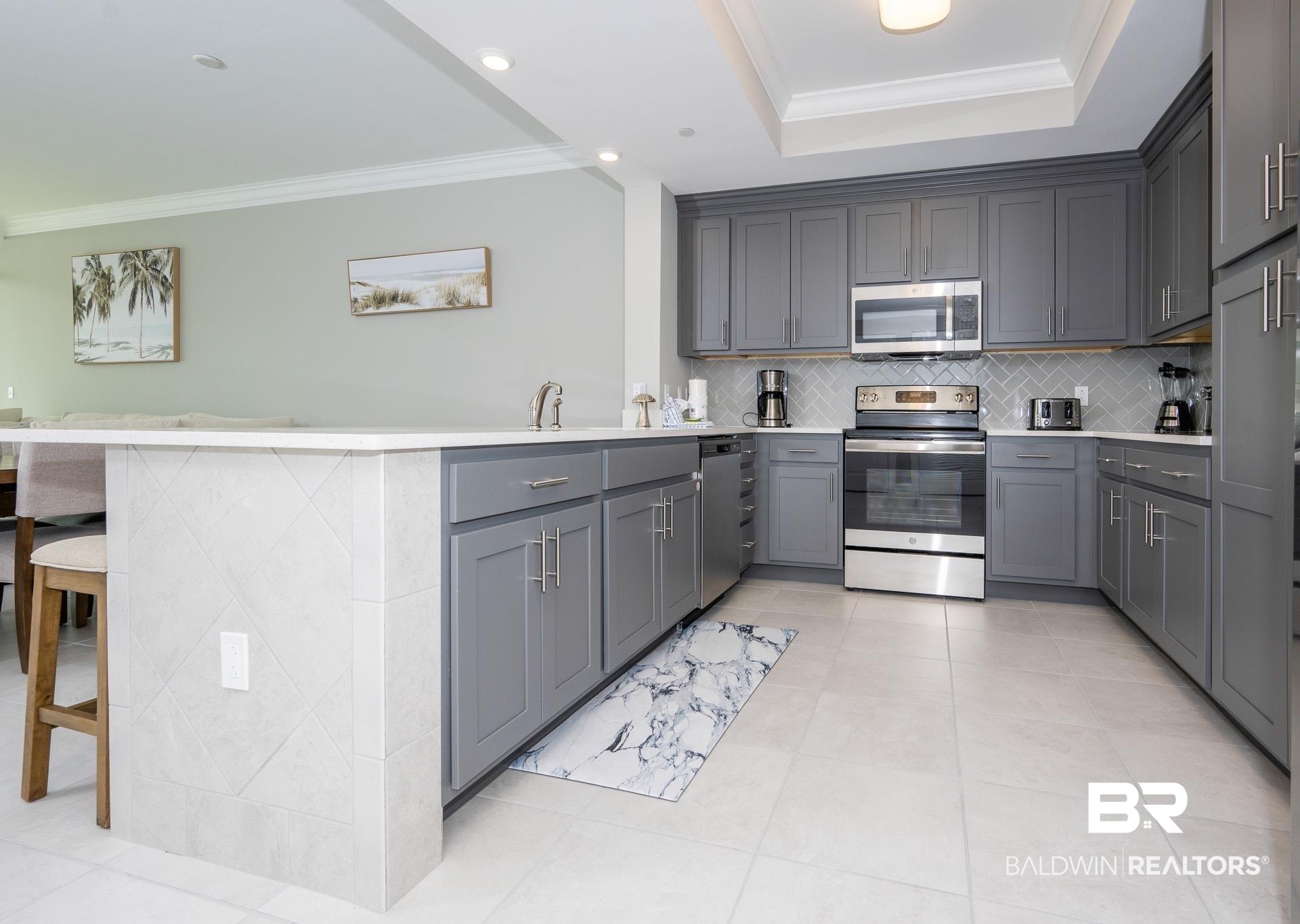 Image 4: Kitchen featuring ornamental molding, appliances with stainless steel finishes, tasteful backsplash, gray cabinets, and a peninsula
