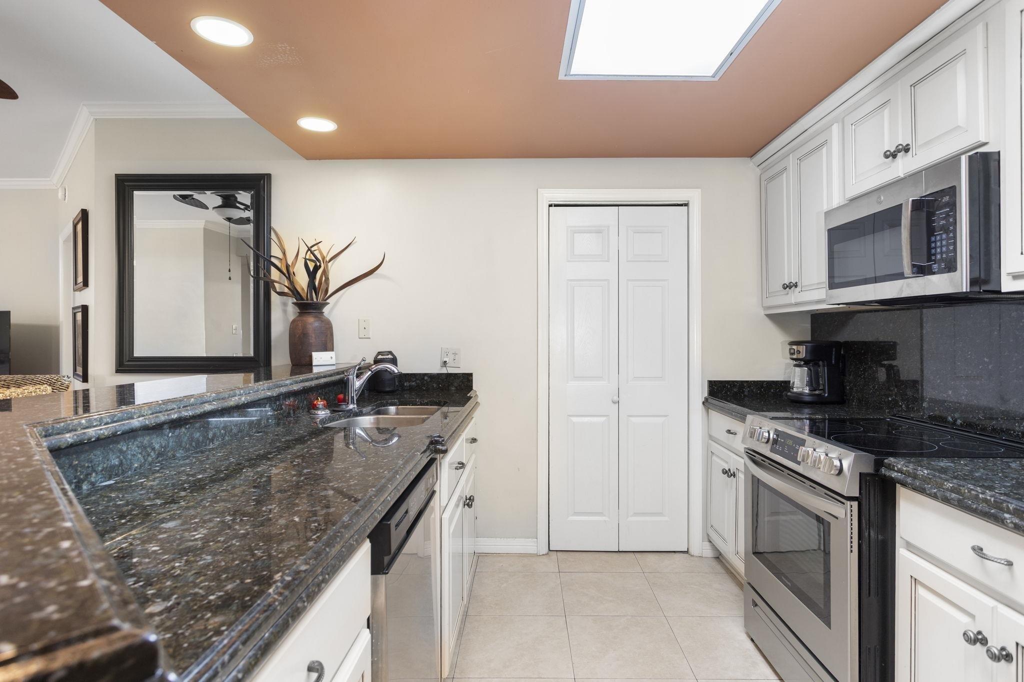 Image 3: Kitchen featuring appliances with stainless steel finishes, white cabinets, dark stone countertops, light tile patterned flooring, and recessed lighting