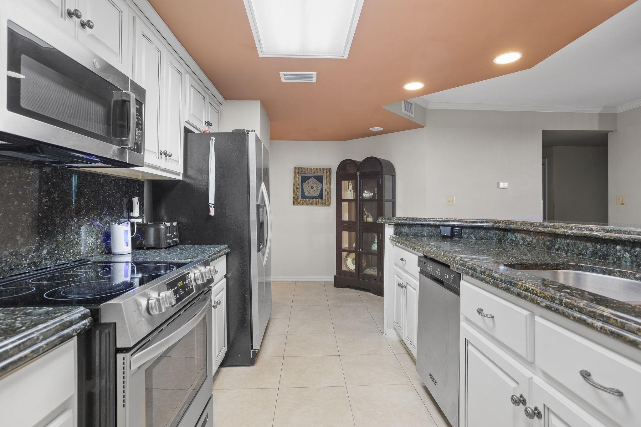 Image 4: Kitchen with white cabinetry, appliances with stainless steel finishes, dark stone countertops, recessed lighting, and light tile patterned floors
