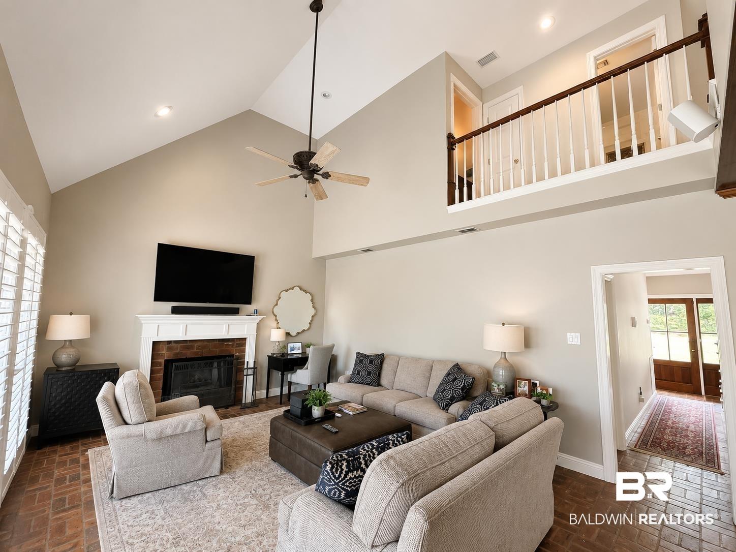 Image 4: Living room featuring a vaulted ceiling with a ceiling fan, brick fireplace with a white mantel, and brick-finish flooring