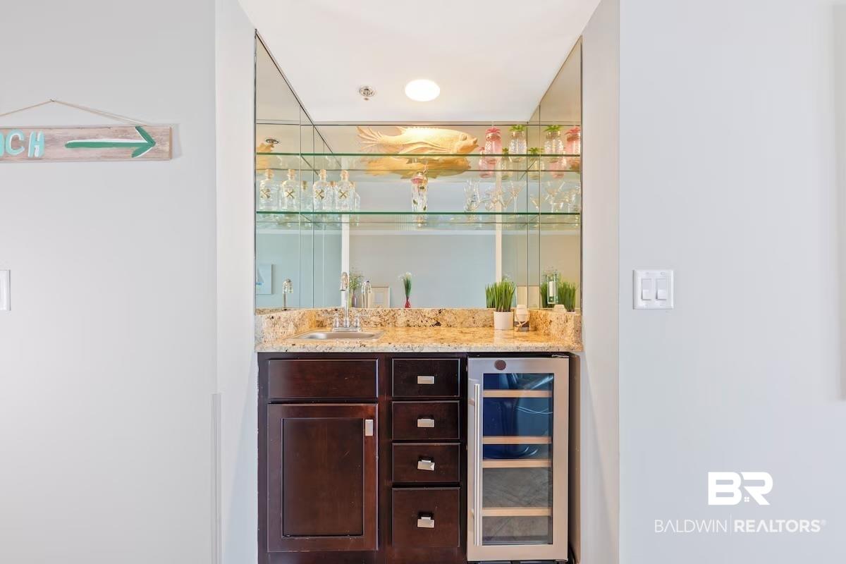 Image 4: Indoor wet bar with dark wood finish cabinetry, wine cooler, and light stone counters