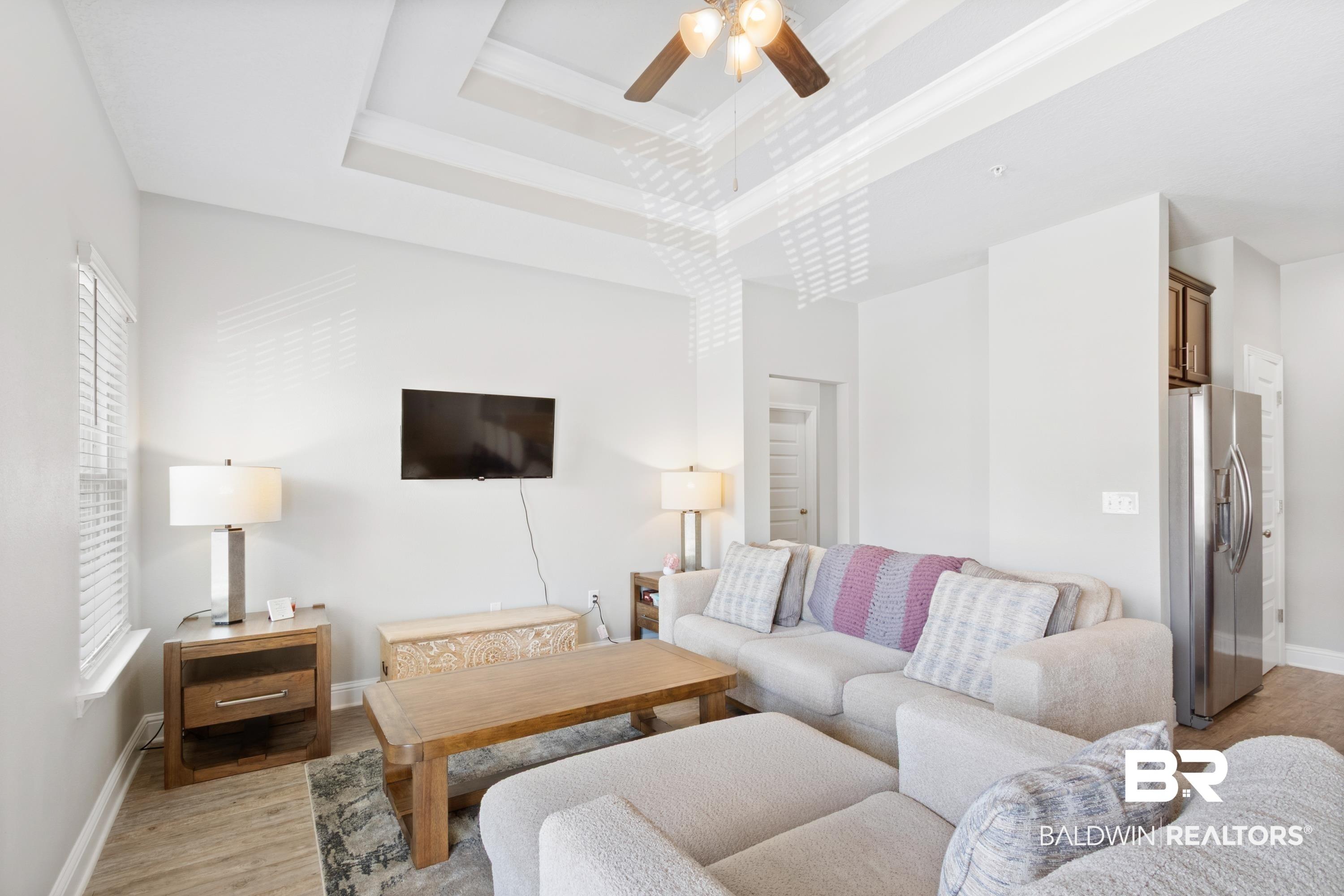 Image 3: Living area featuring a ceiling fan, light wood-style flooring, and a high tray ceiling