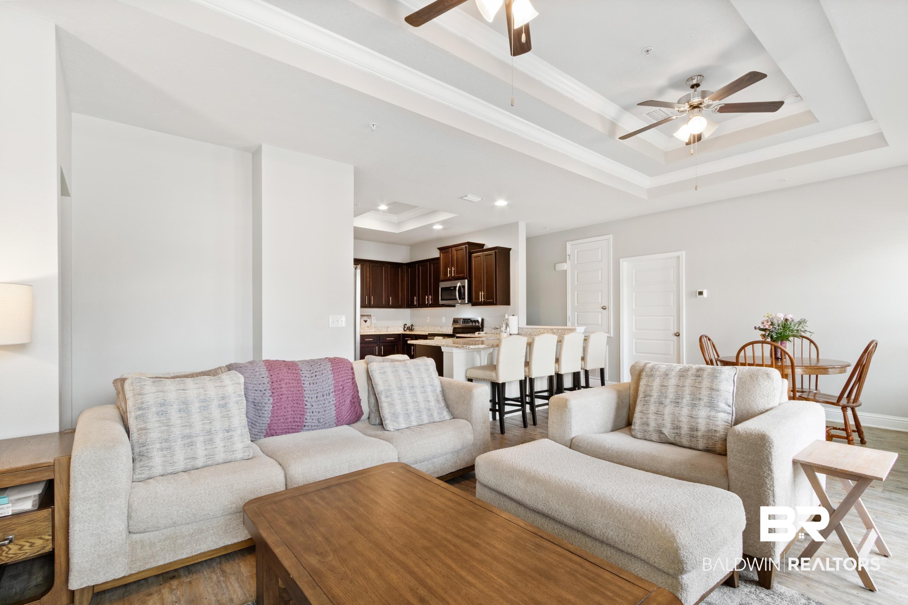 Image 4: Living area featuring light wood-type flooring, a ceiling fan, a raised ceiling, and crown molding