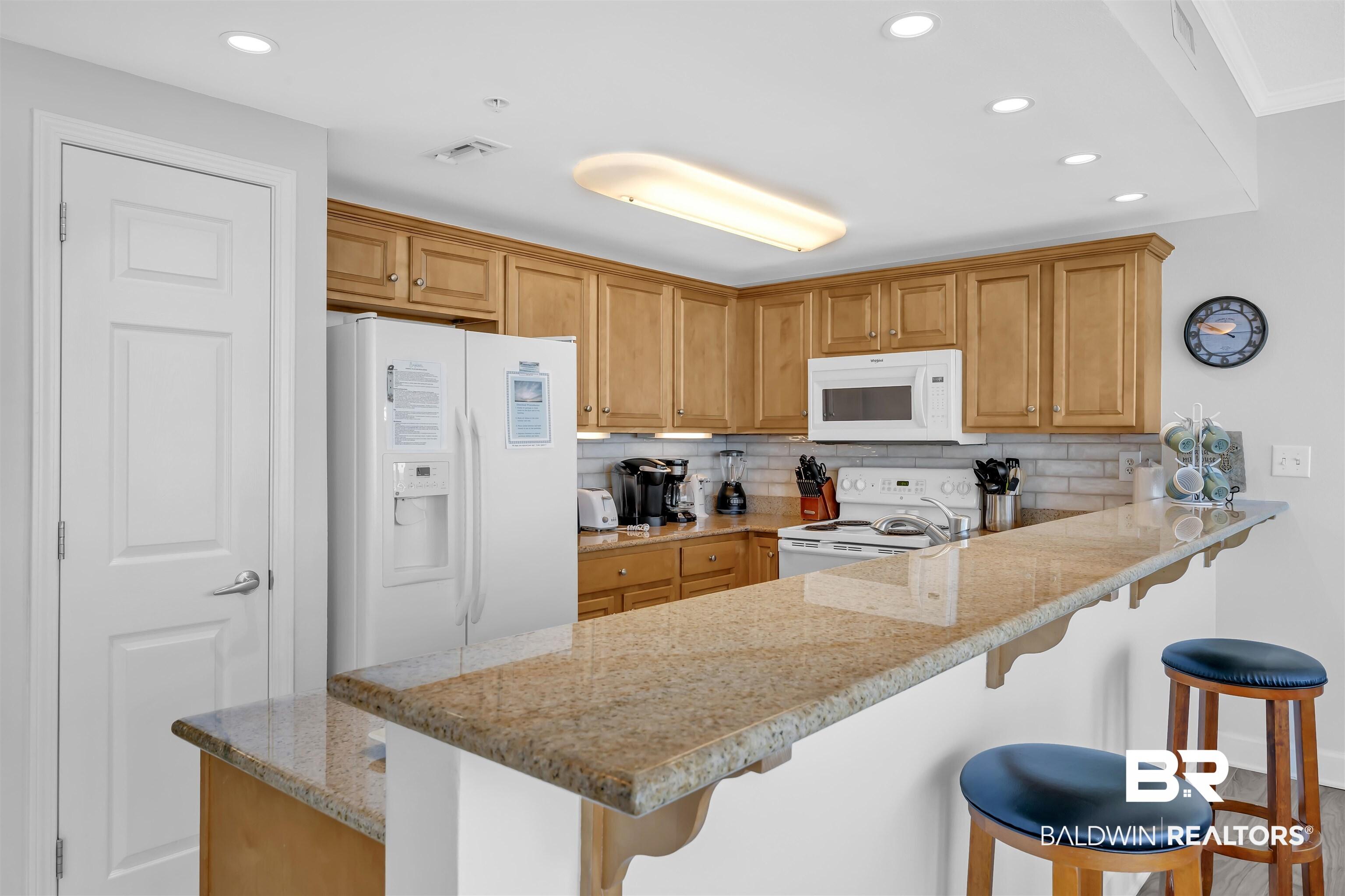Image 4: Kitchen featuring a kitchen breakfast bar, white appliances, light stone counters, tasteful backsplash, and a peninsula