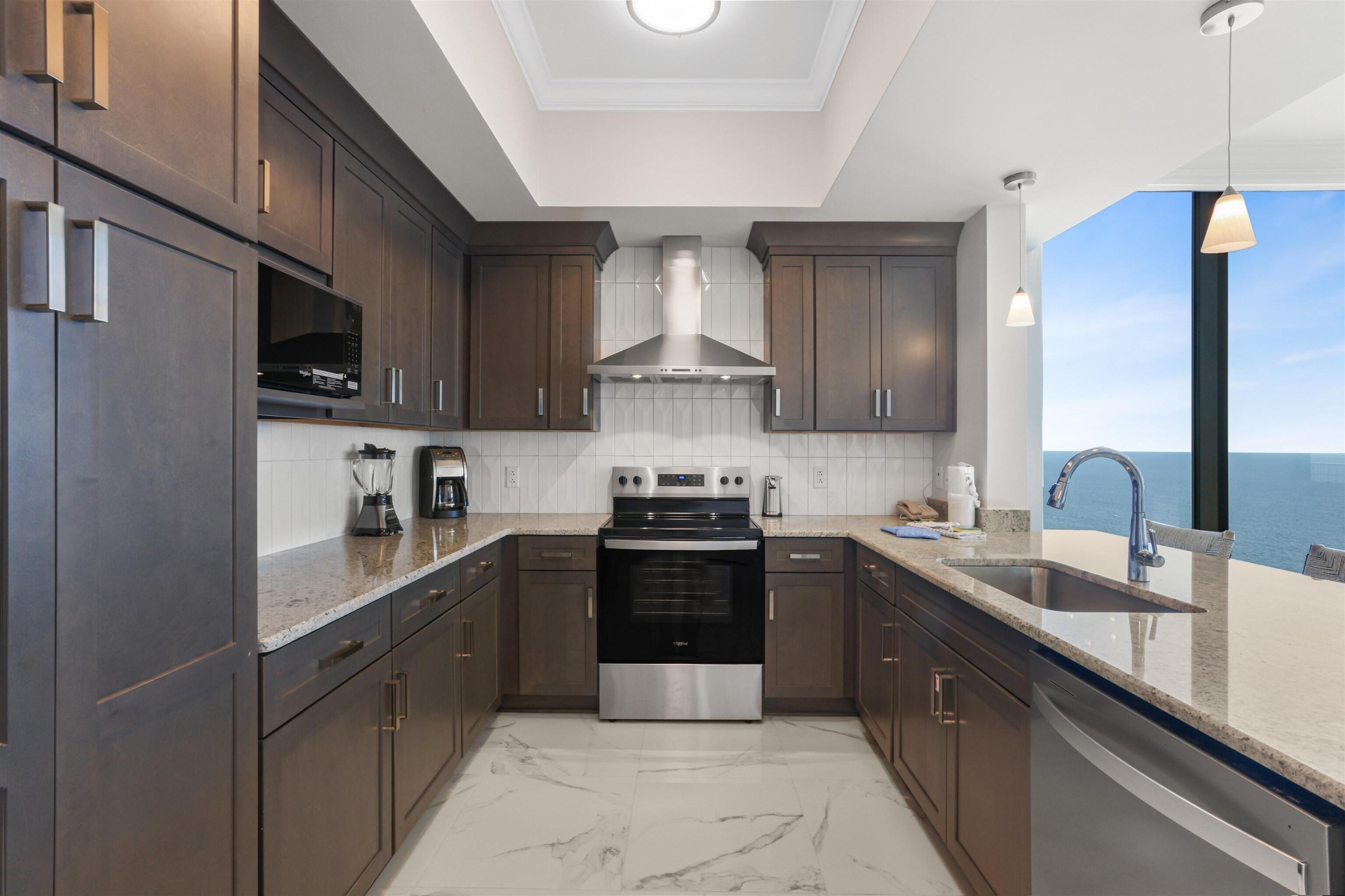 Image 3: Kitchen featuring a raised ceiling, backsplash, stainless steel appliances, wall chimney exhaust hood, and dark brown cabinets