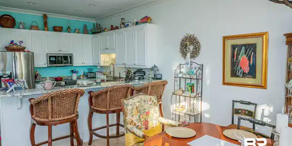 Image 3: Kitchen featuring light stone countertops, stainless steel appliances, white cabinetry, a kitchen breakfast bar, and ornamental molding