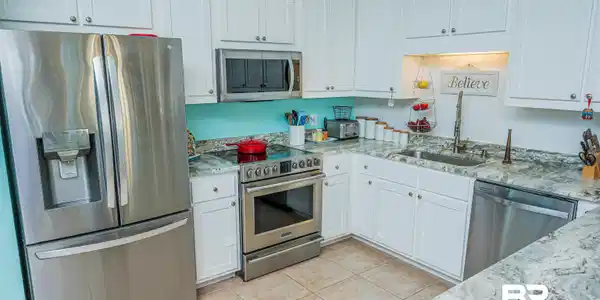 Image 4: Kitchen with stainless steel appliances, light stone counters, white cabinetry, and light tile patterned floors