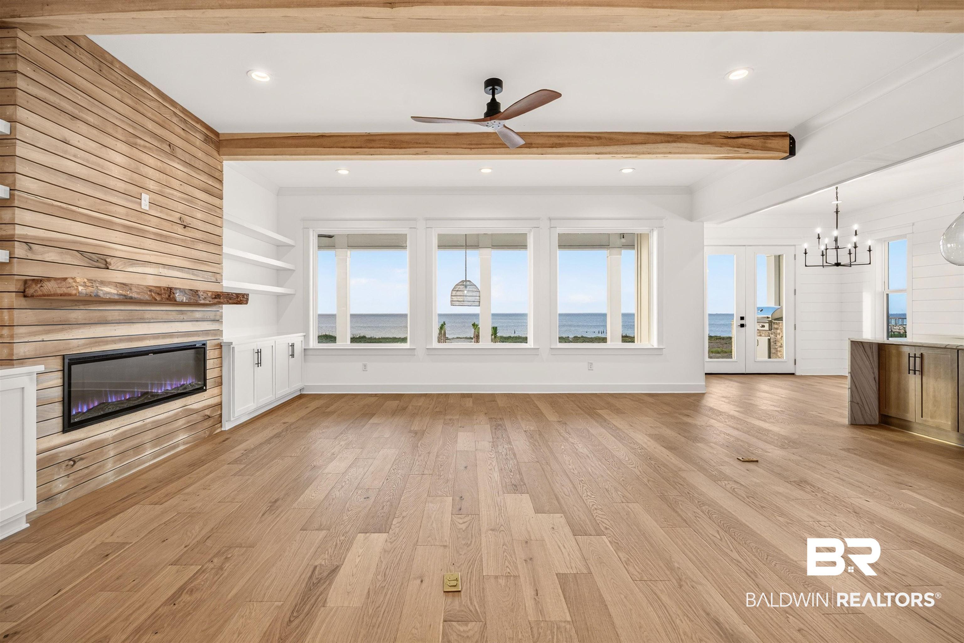 Image 4: Open-concept living area featuring wide-plank wood-finish flooring, a linear electric fireplace with a wood-plank accent wall and floating mantel, and built-in shelving