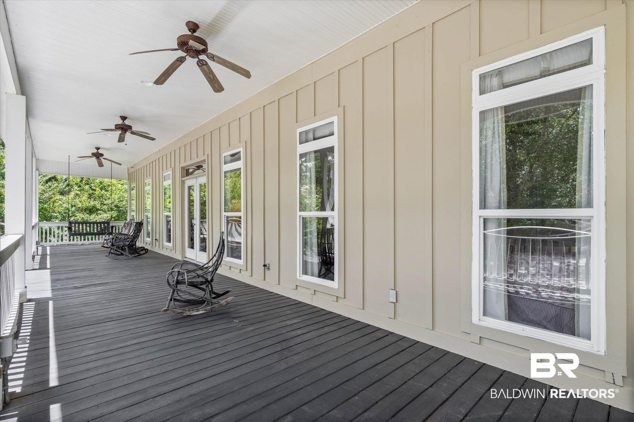Image 2: Expansive covered porch featuring dark wood-finish decking, multiple ceiling fans, and board and batten siding