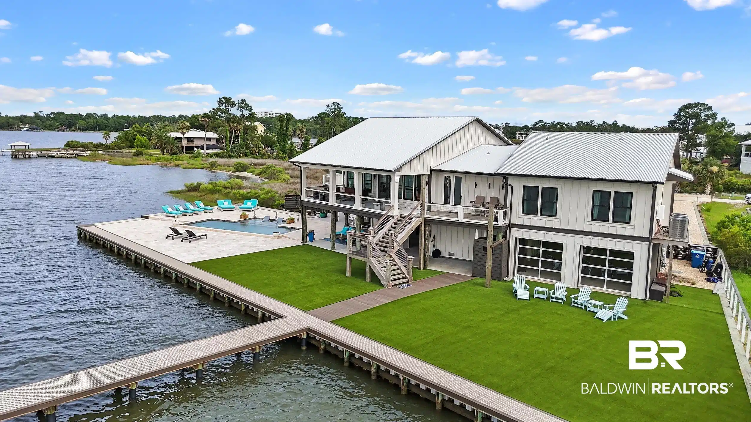 Image 1: Waterfront residence featuring a private dock, expansive waterside patio, in-ground swimming pool, artificial turf lawn, and a two-story exterior with multiple balconies