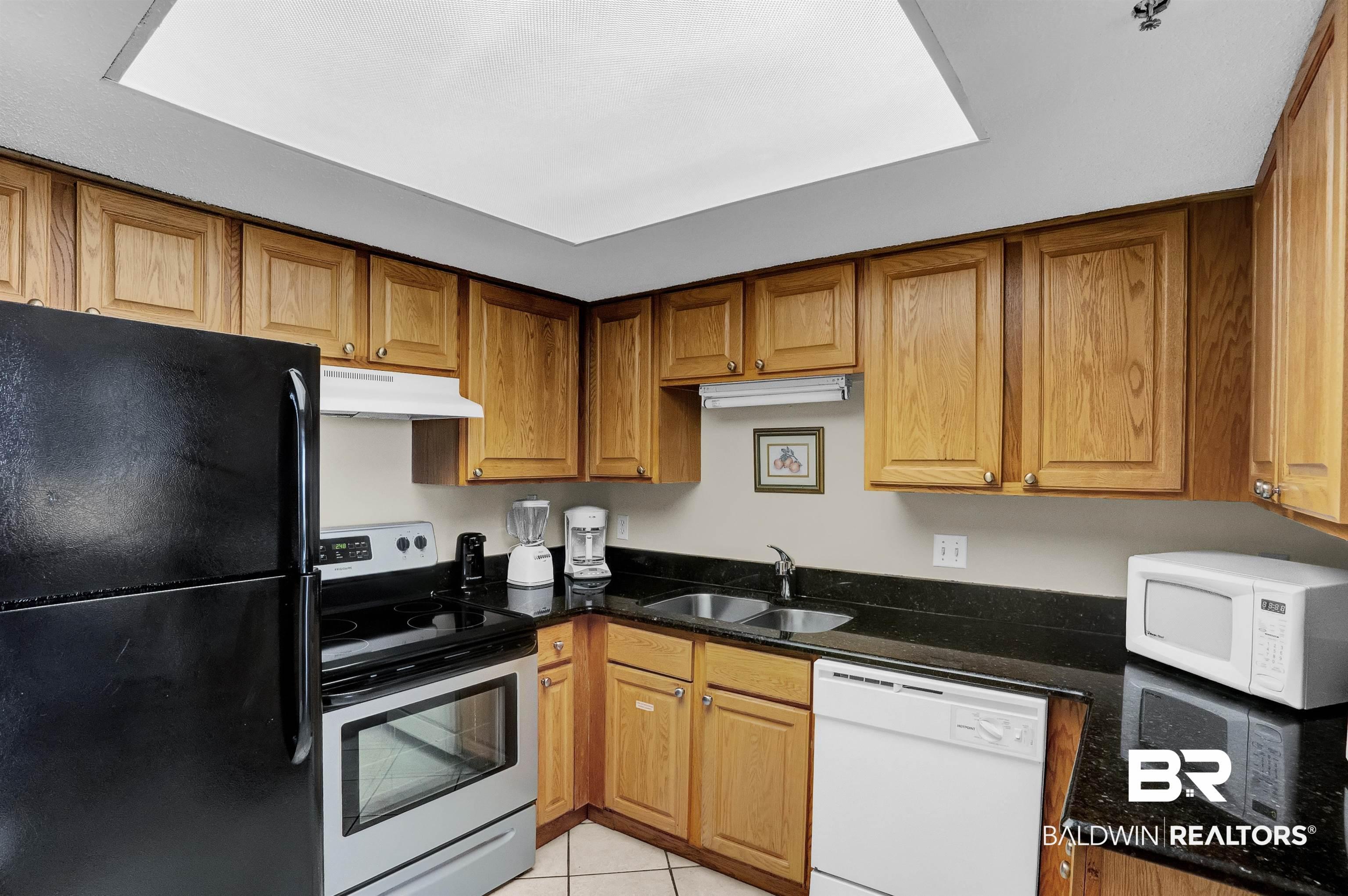 Image 2: Kitchen with white appliances, light tile patterned floors, a sink, under cabinet range hood, and brown cabinets