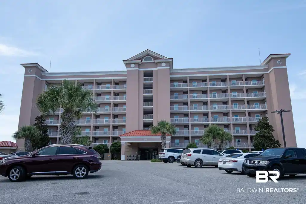 Image 1: Multi-story building featuring numerous private balconies, a central arched entrance, a parking lot, and mature palm trees