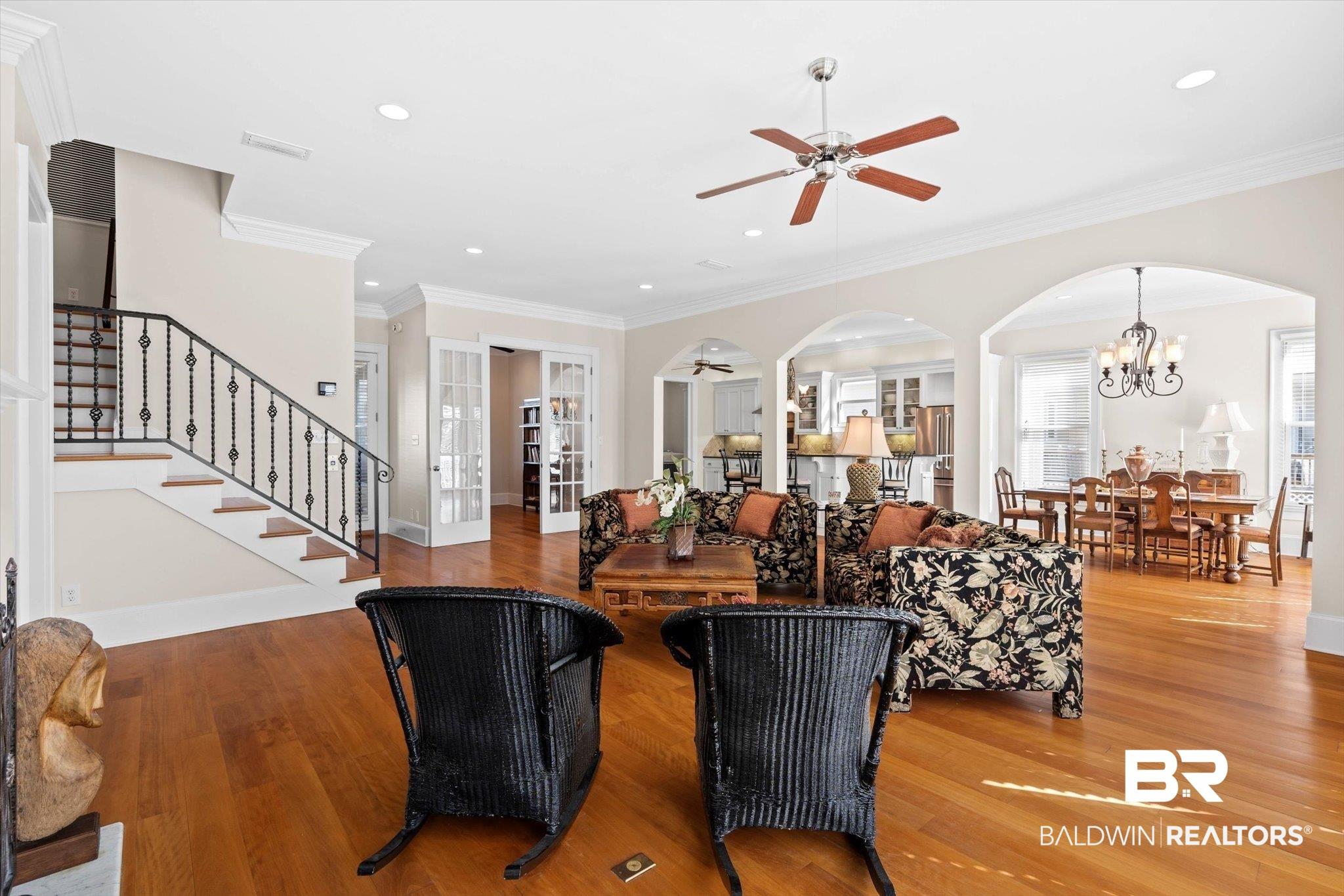 Image 2: Living area with stairs, arched walkways, ornamental molding, wood finished floors, and a chandelier