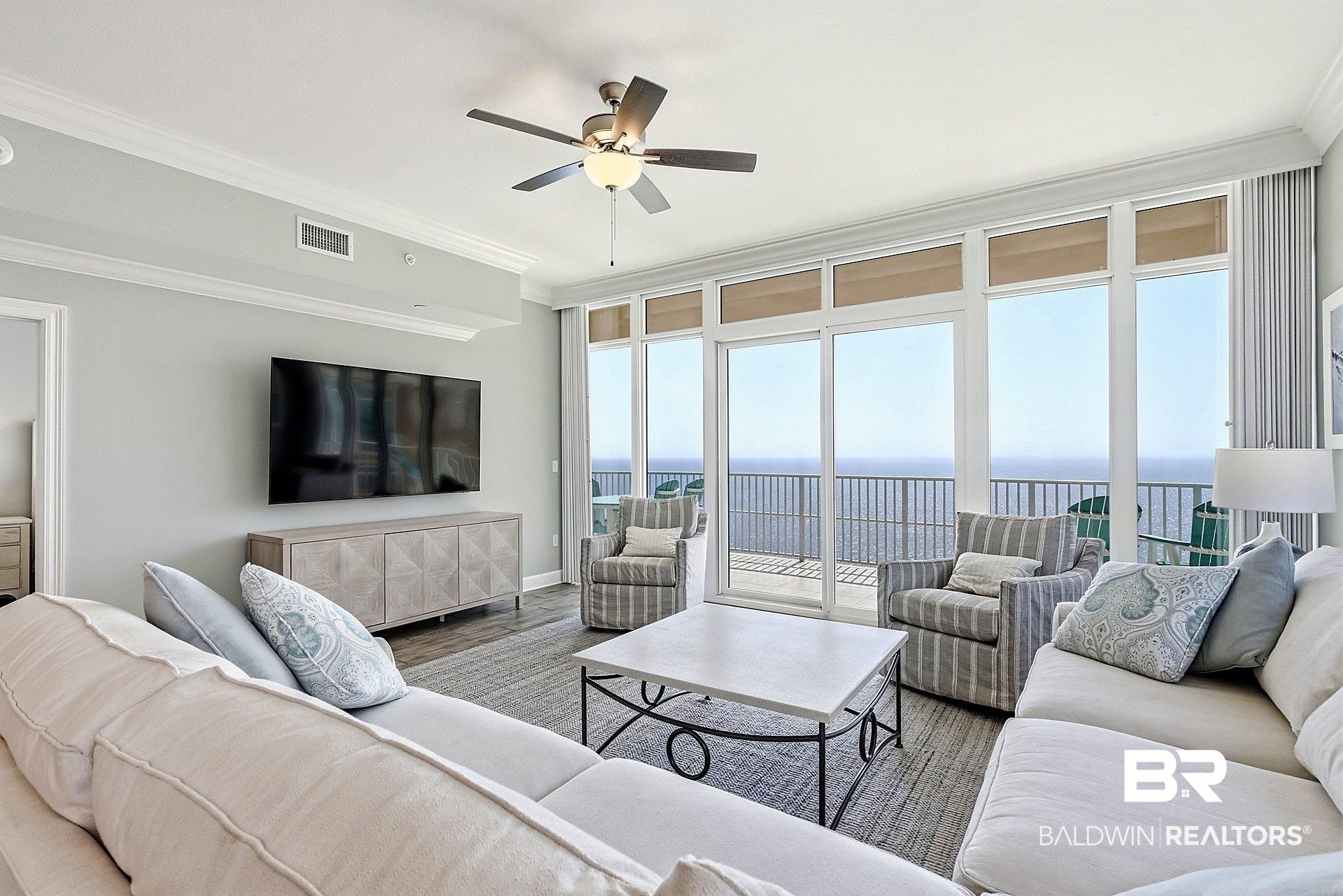 Image 4: Living area with ornamental molding, a ceiling fan, wood finished floors, and expansive windows